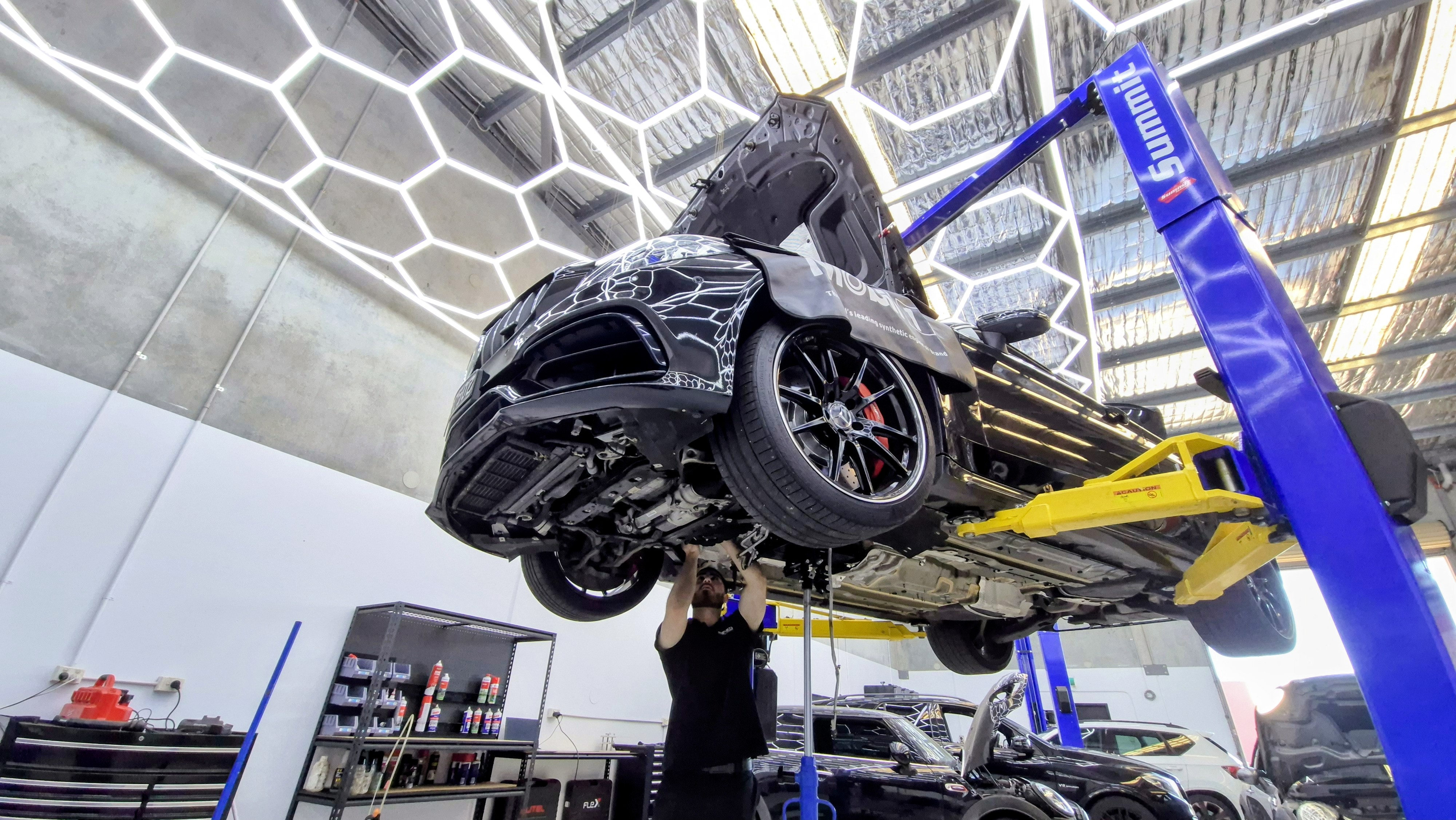 Amped technician working underneath a Mercedes-AMG C63 on the workshop hoist